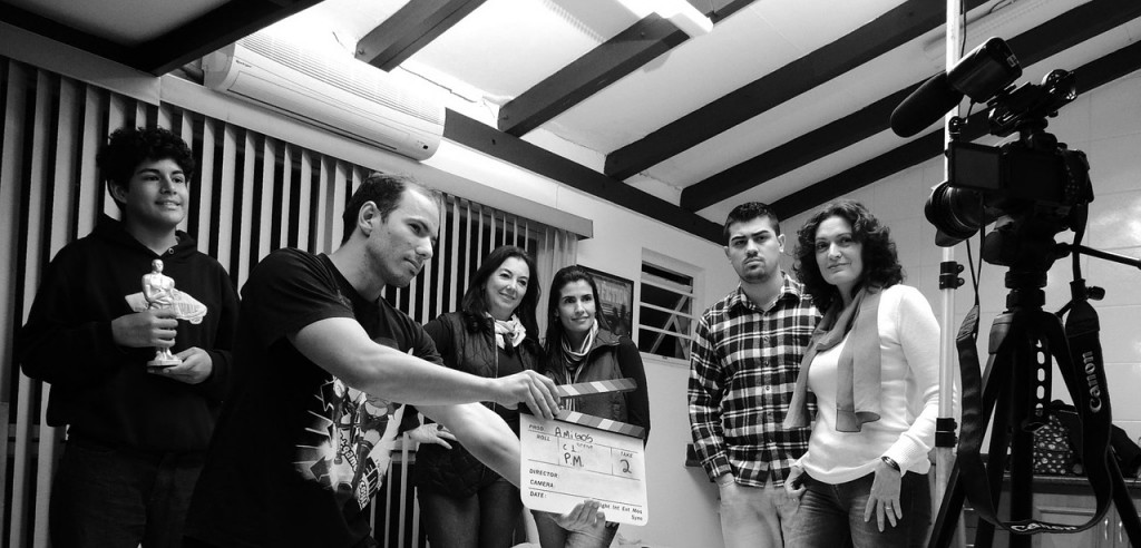 A group of people standing in front of a movie camera on a tripod. A man stands in front of them holding a clapperboard.