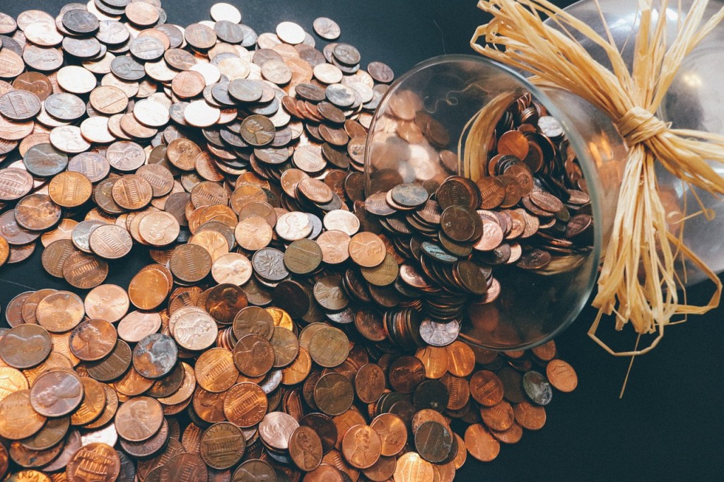 A glass vase tipped over with hundreds of pennies spilling out of it.