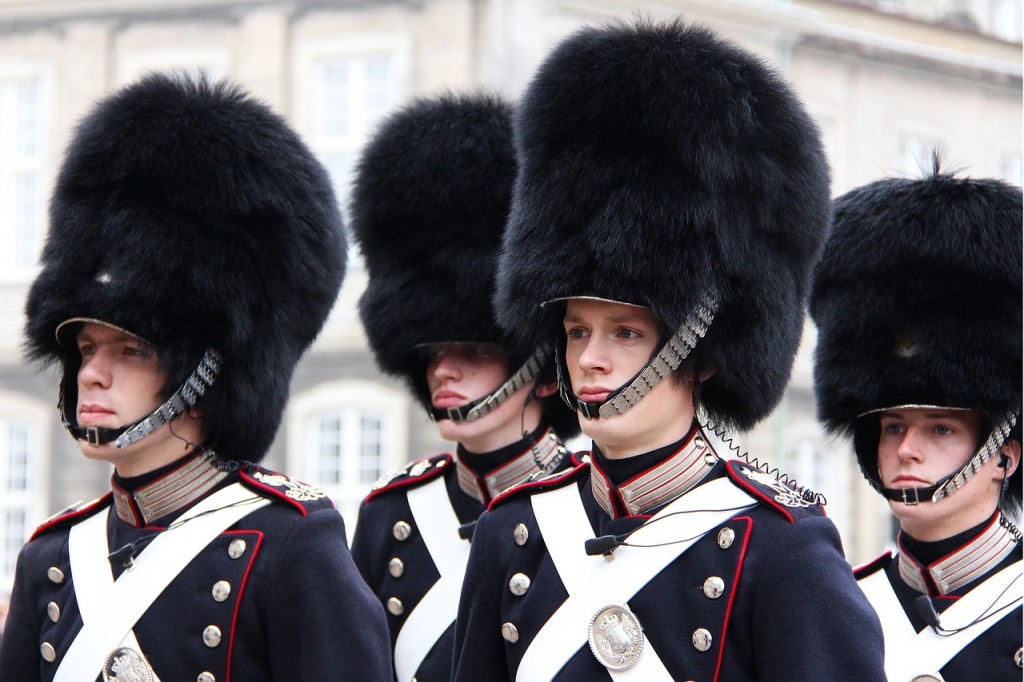 4 Royal Guards on the square at Amalienborg Castle. They have navy and white uniforms and enormous black, fuzzy hats.