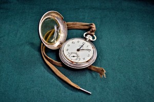 An old pocket watch with the case open and brown shoe lace tied to it.