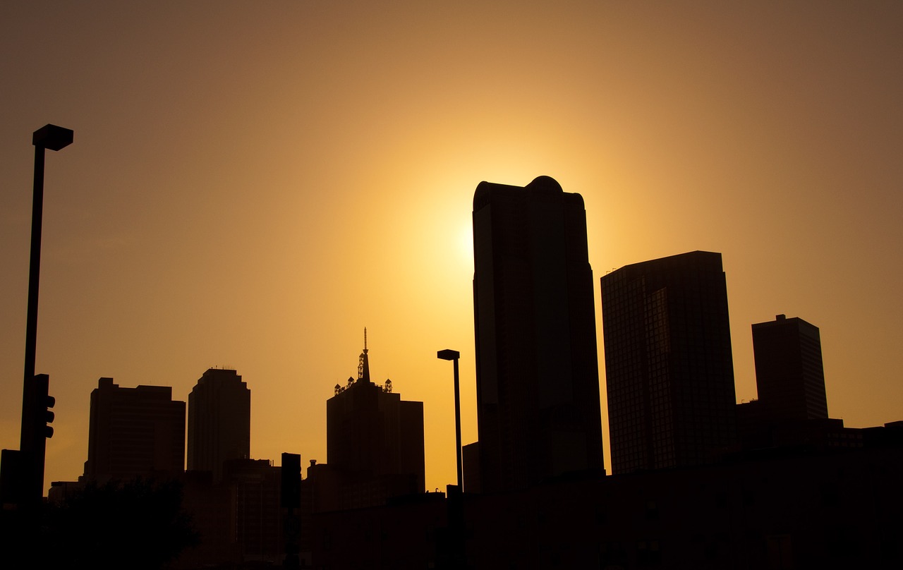 The Dallas skyline in silhoutte with the sun setting behind the buildings.