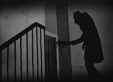 Shadow of a creepy man reaching towards a door at the top of a staircase.