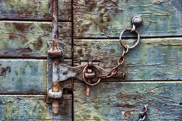 A weathered, blue door locked with a large chain and a padlock.