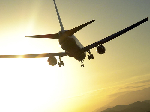 An airplane flying towards a setting sun.