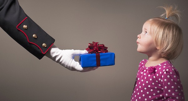 A uniformed arm holding out a gift to a little girl in a pink dress.