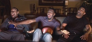 3 men sitting on a couch watching football and reacting excitedly.