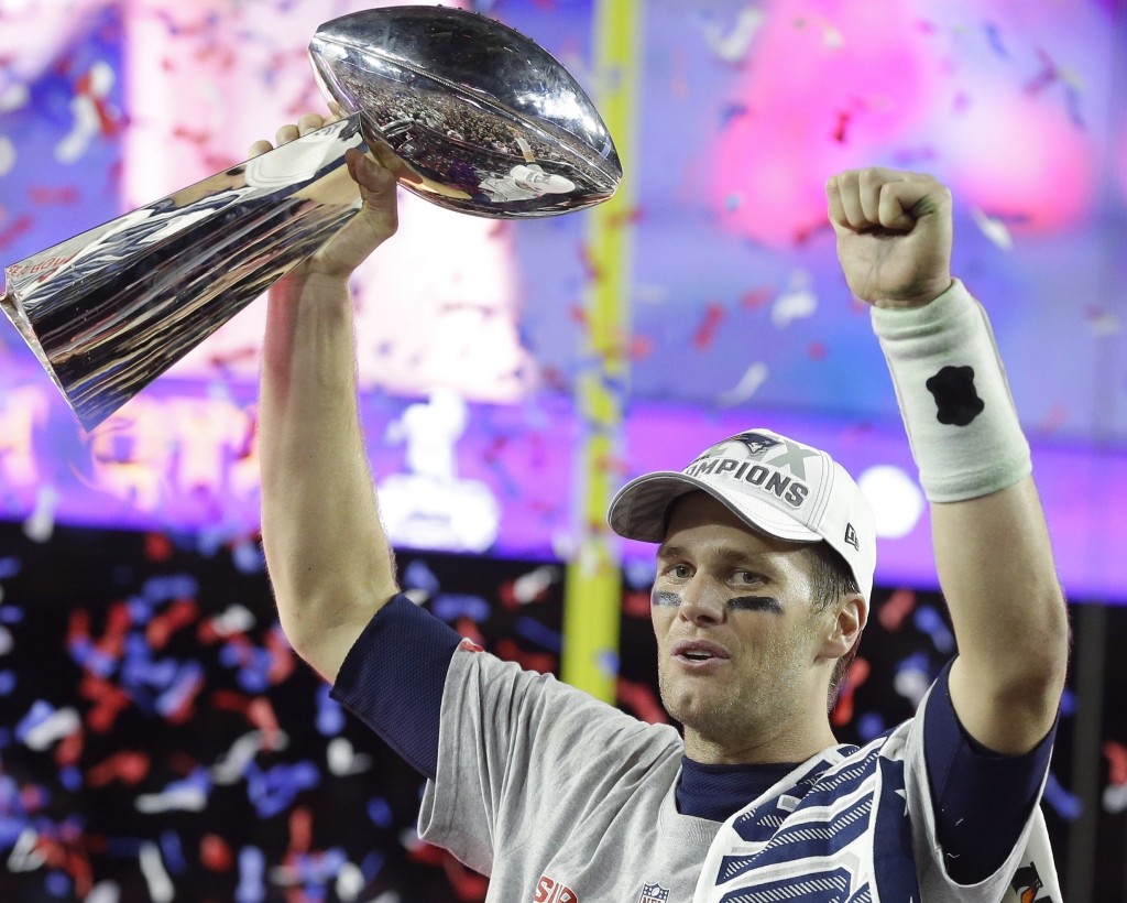 Tom Brady holding up a Super Bowl trophy in a crowded stadium.