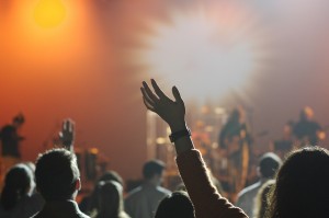 An audience, some with hands raised in the air, in front of a band on stage.