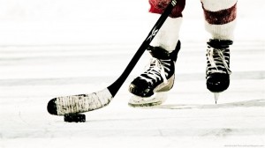 The feet of a hockey player with the hockey stick about to hit the puck.
