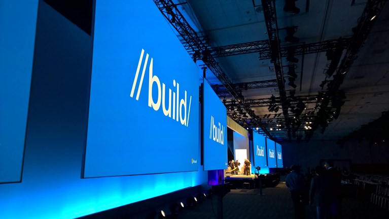 A mostly empty theatre room with many screen across the stage. The screens are blue and say build.