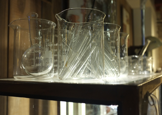 Several beakers, test tubes and other glass containers with measurements, sitting on a shelf.