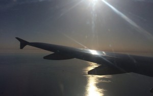 The wing of a plane over water with the sun shining on it.