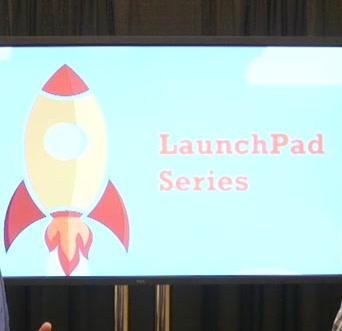 A large screen at the front of a room showing a rocket and the words Launch Pad series.