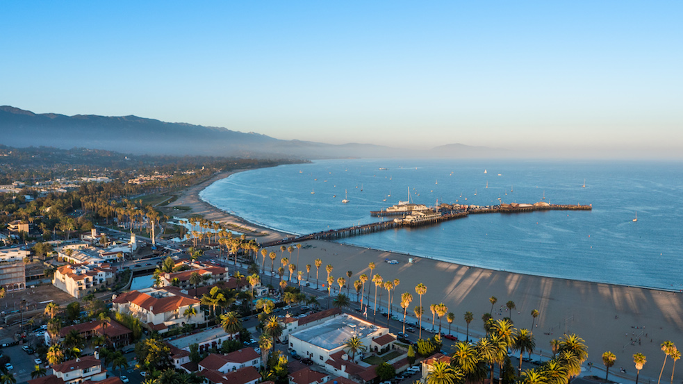 A town right on the beach with lots of palm trees and sail boats in the bay.