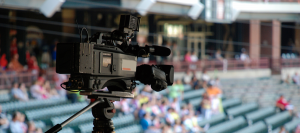 Photograph of a video camera on a tripod at an outdoor sporting event.