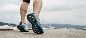 A man's legs as he's jogging towards snowy mountains in the distance.