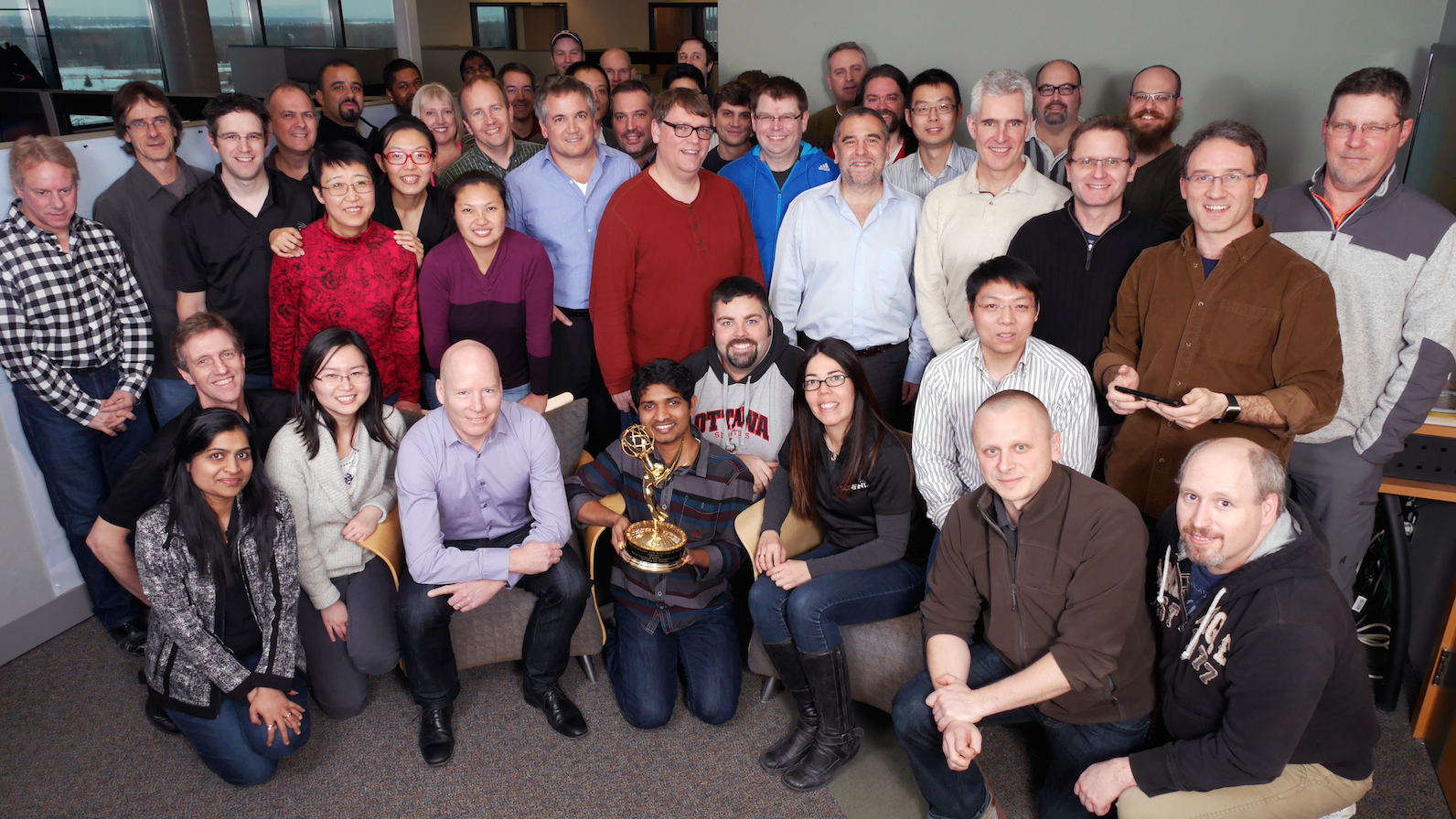 A big group of people in an office in Ottawa. The man in the center is holding an Emmy award.
