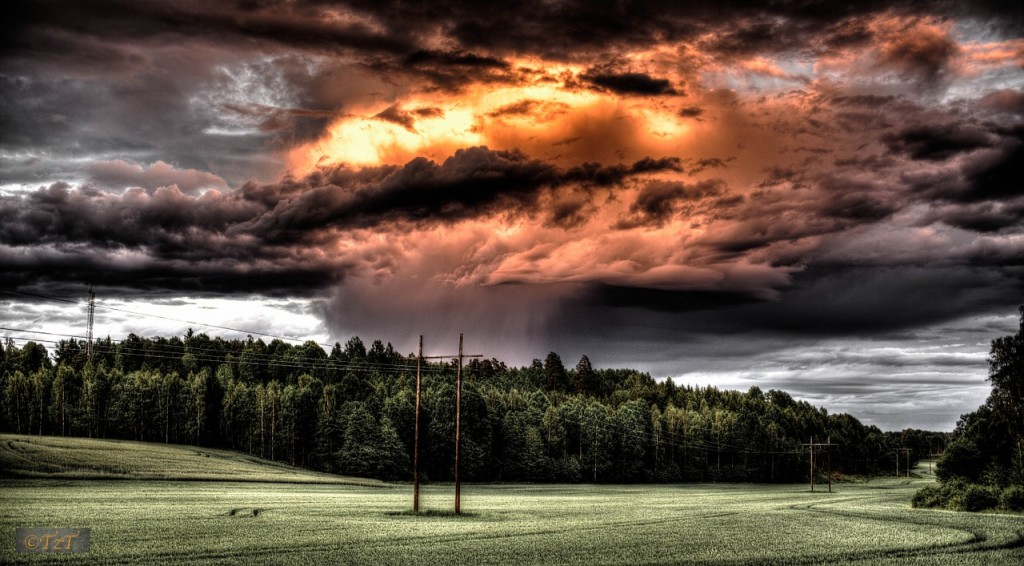 A dark, but beautiful storm rolling in over a forest and clearing, with power lines in the clearing.