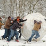 A bunch of college age men rolling an enormous snowball.