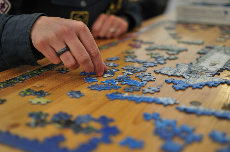 A person putting together a large jig saw puzzle on a table.