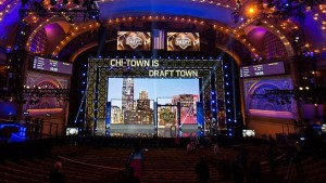 A mostly empty theater with many screens on and around the stage and a sign that says Chi Town is Draft Town.