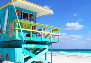 A bright blue, green and yellow surf shack on a beach.