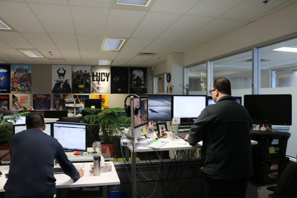 2 men working on film editing. The wall in front of them is covered in movie posters.