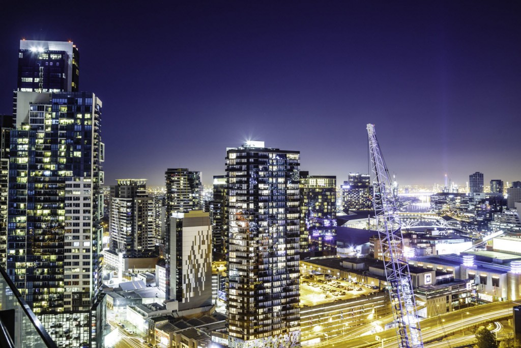 A large city with skyscrapers, a crane, a sports stadium and a parking garage, all lit up at night.