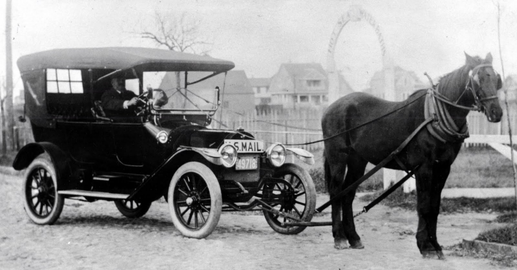 A man driving a model T Ford with a horse hooked up to the front of it.