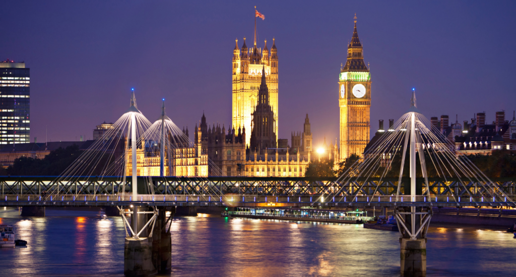 Big Ben and the bridge of the Thames river at night with lots of lights.