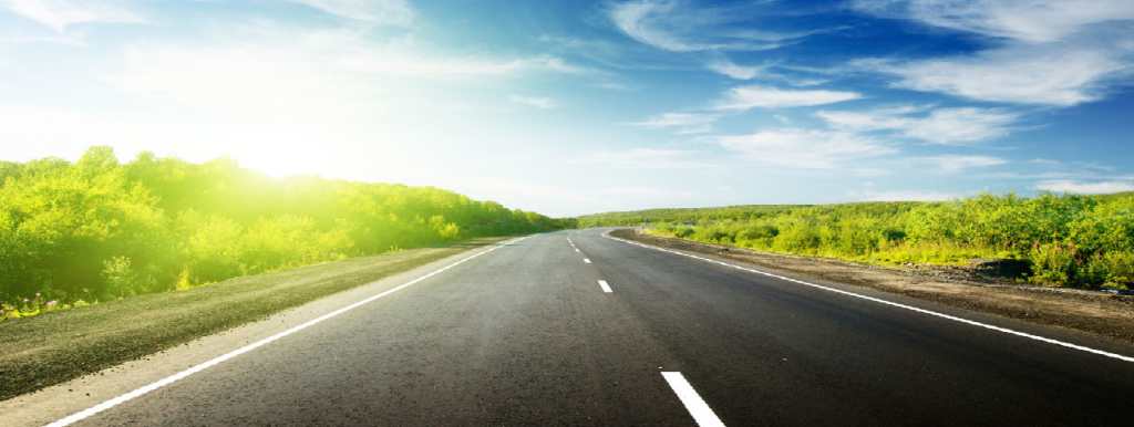 An empty two lane road cutting between green fields.