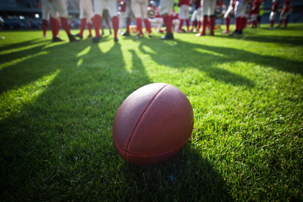 A football on a football field with a team standing in the background.