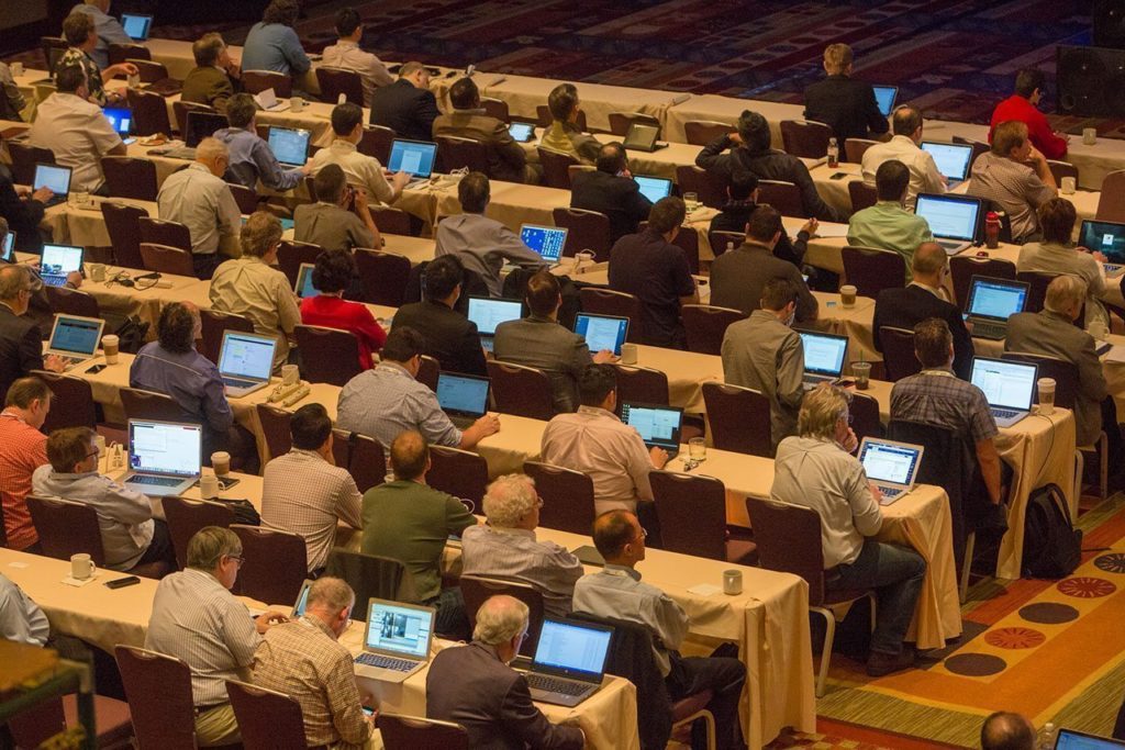 A large group of people sitting at tables, working on laptops at an HPA Tech convention.