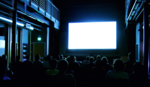 People in a small movie theatre, but the screen is just glowing white.