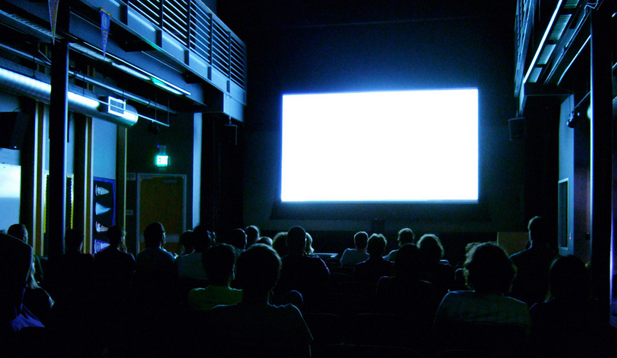 People in a small movie theatre, but the screen is just glowing white.