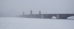 A long bridge over a large body of water in the fog.