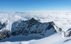 A beautiful, snowy mountain with other mountain peaks behind it, coming up through the clouds.