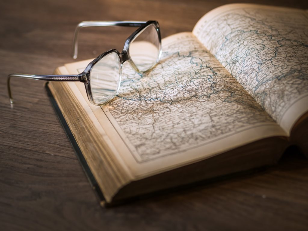 A book of maps open with a pair of glasses on the book.
