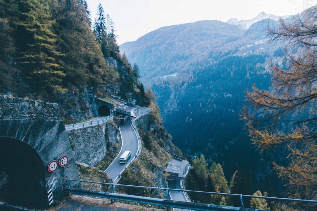 Cars driving on winding roads and tunnels on a mountain side during autumn.
