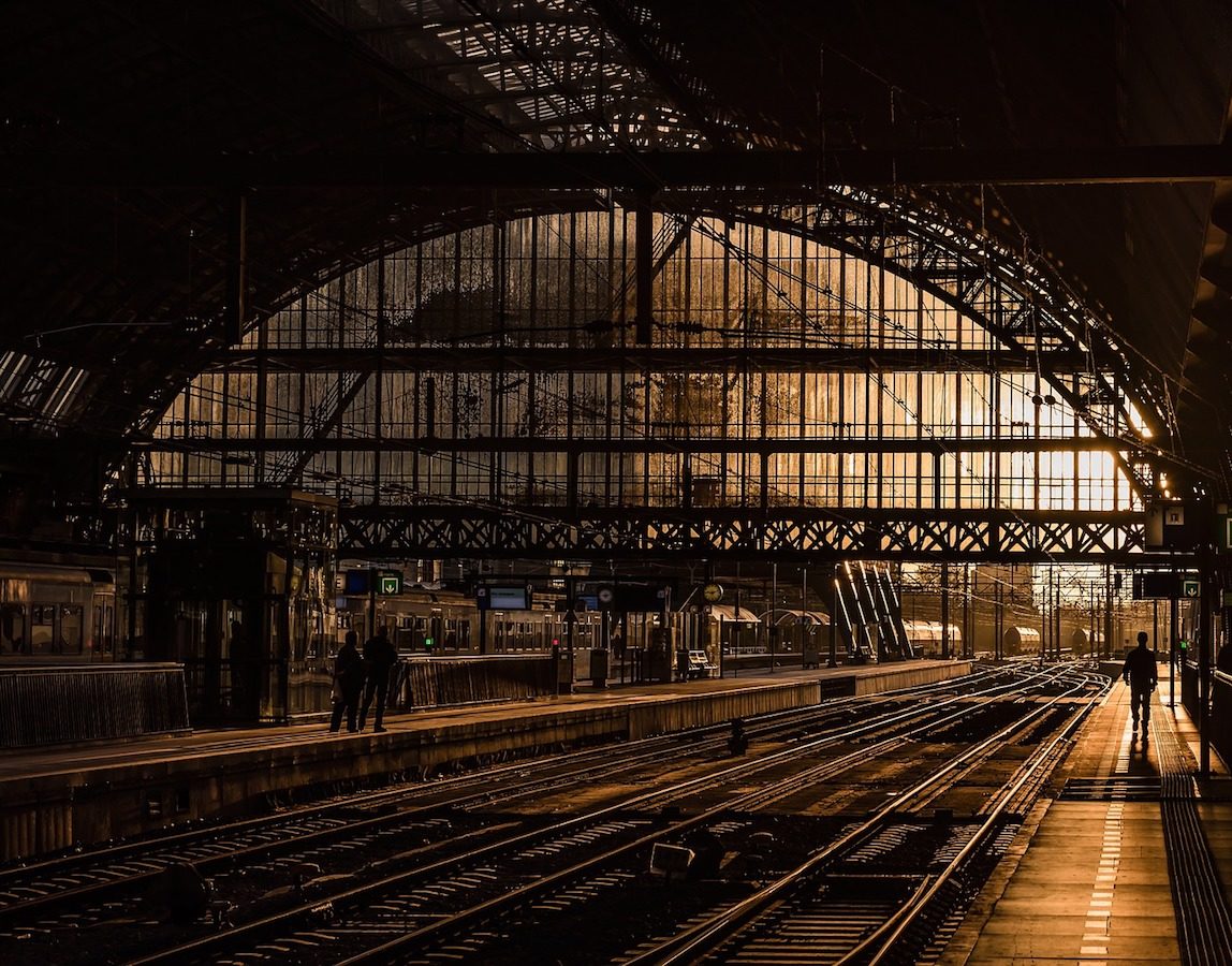 A large train station with no trains and only a few people standing around.