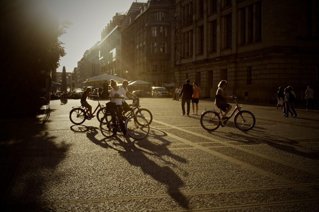 People riding bikes and walking down a street in the summer sunshine.