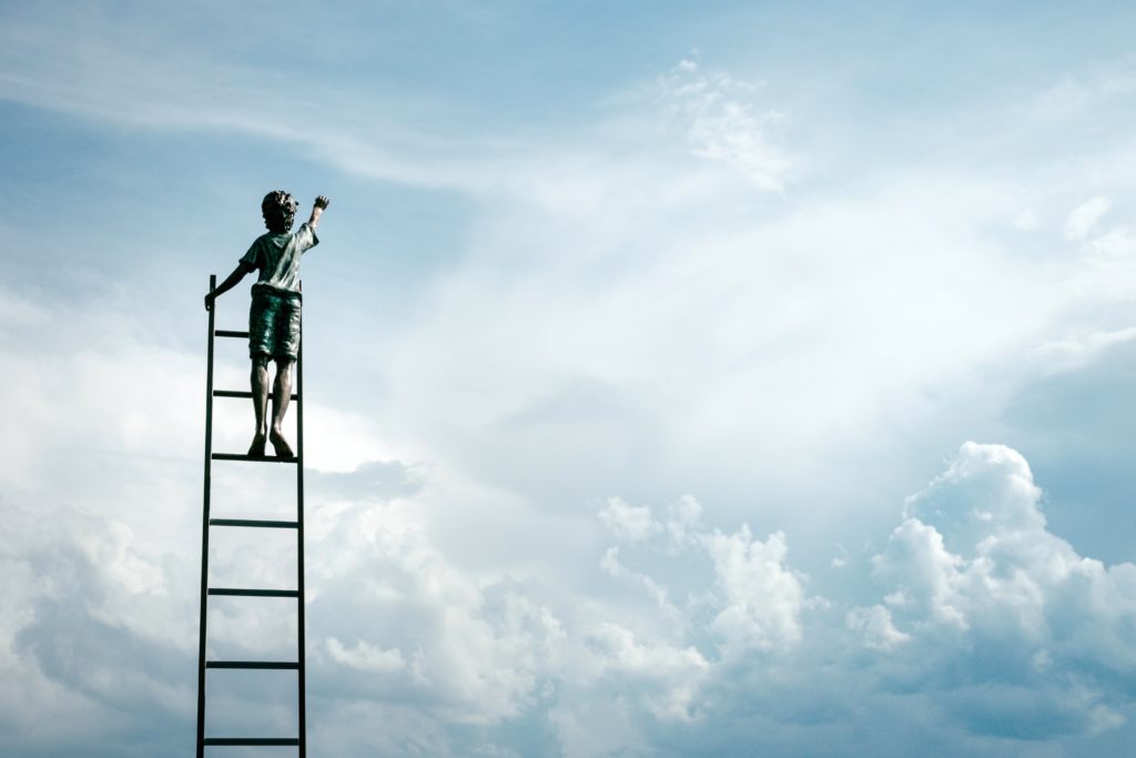 A sculpture of a child at the top of a ladder reading towards the sky.