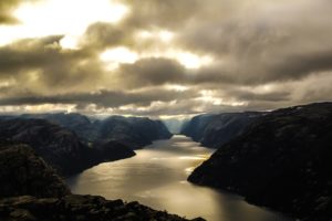 A fjord in Norway under a cloudy sky, but with a few beams of sunlight breaking through.