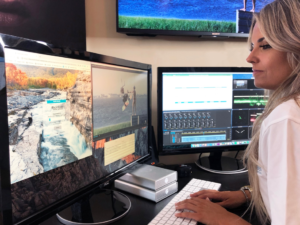 Working at her desk on her computer with 2 monitors.