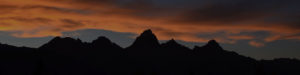 A mountain range at dusk, with the sun behind it.