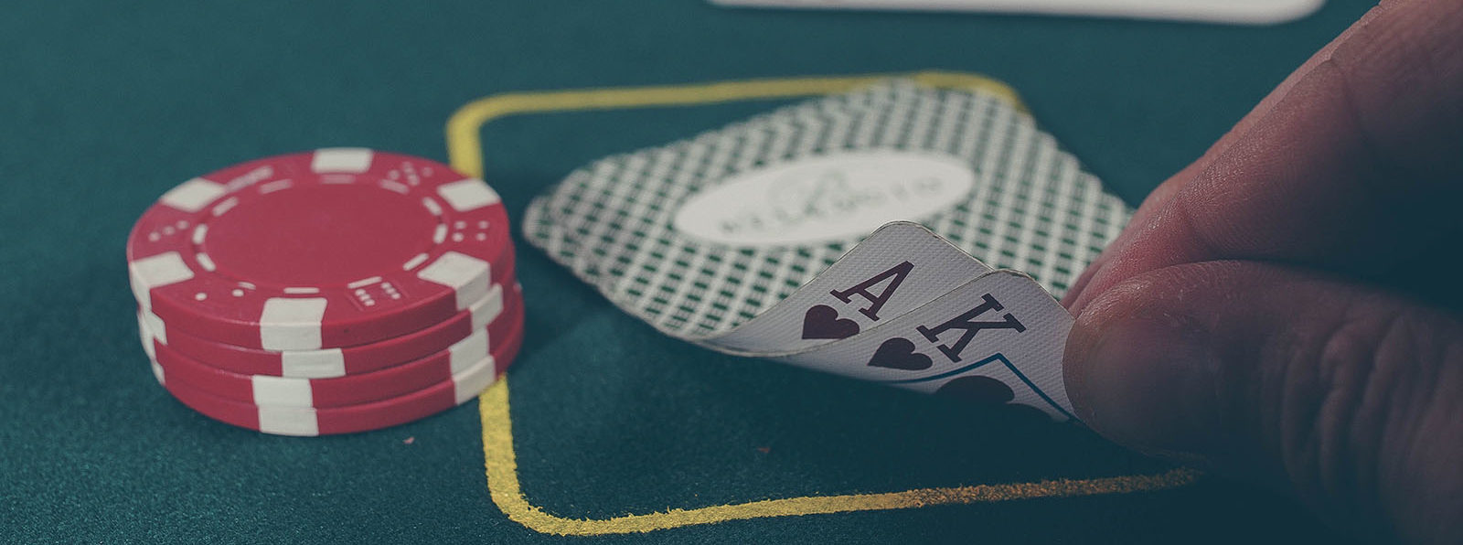 2 red poker chips next to fingers holding up the corner of playing cards to show that they are an Ace and King of hearts.