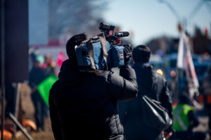 A man filming a parade for a broadcast company.