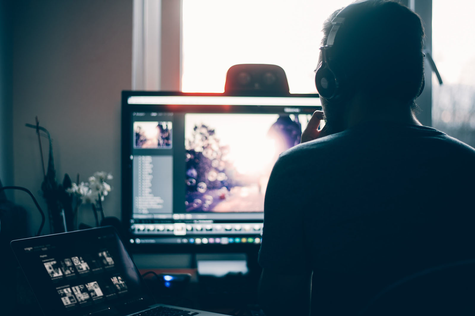 A man working from his home. He has a computer and a laptop on his desk.