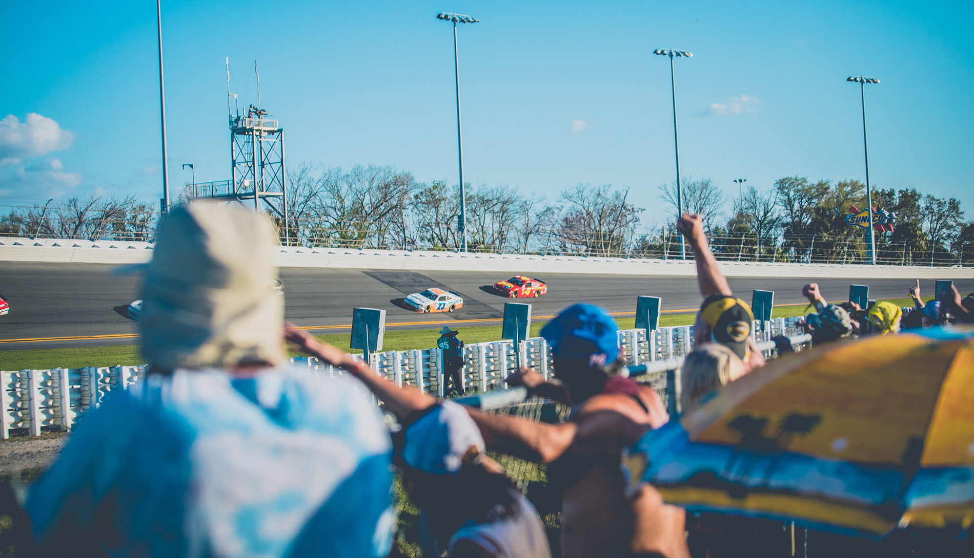 Fans standing at a fence at a Nascar race.