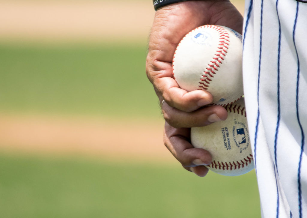 A baseball player holding two baseballs in one hand.